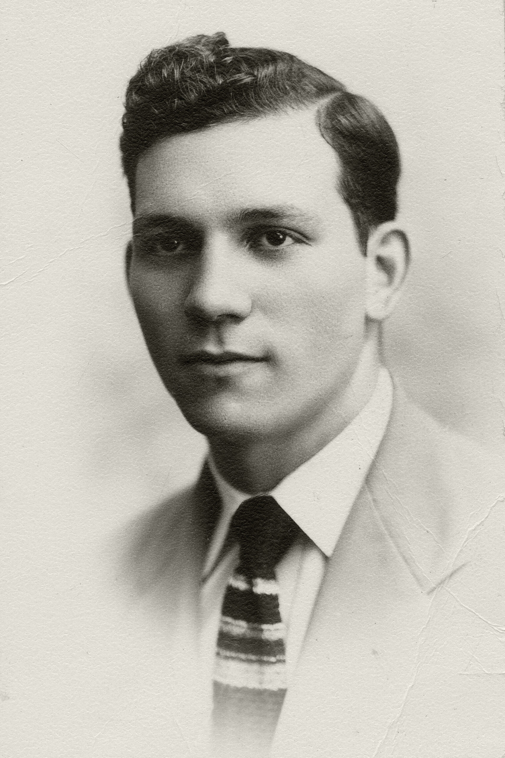 Black and white portrait of a young man in a suit and tie, featuring slicked-back hair and a serious expression, capturing a vintage style
